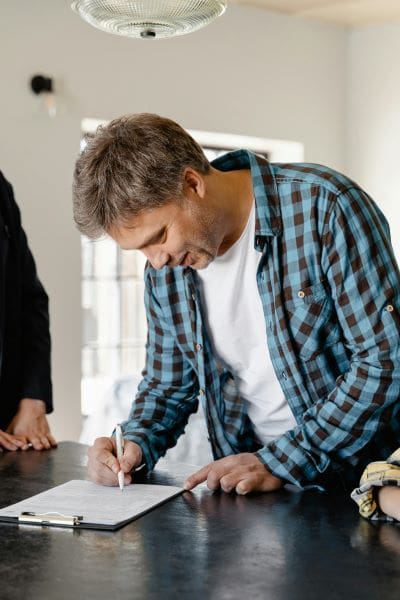 An image of a man signing a document wearing a checkered shirt
