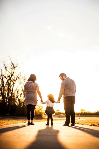 A family of three walking away from the shot at sunset, a mother, child in the middle and father