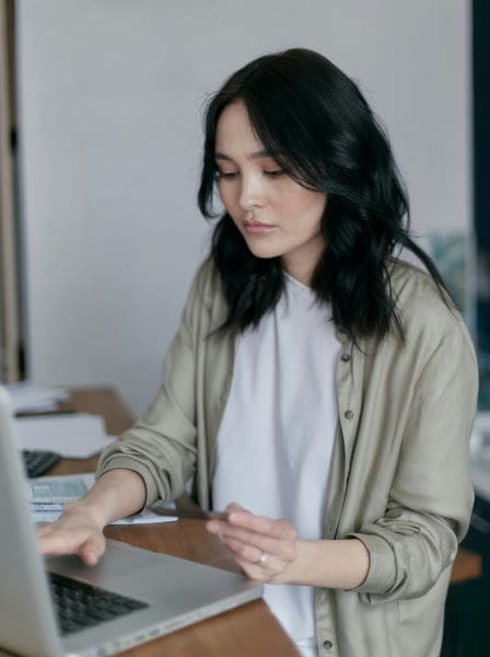 A young Asian lady sitting at a laptop surrounded by paperwork