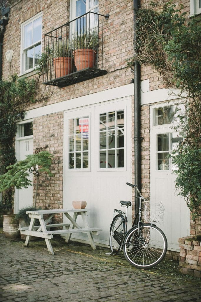 The outside of a light bricked apartment building with a bench and bicycle sitting outside