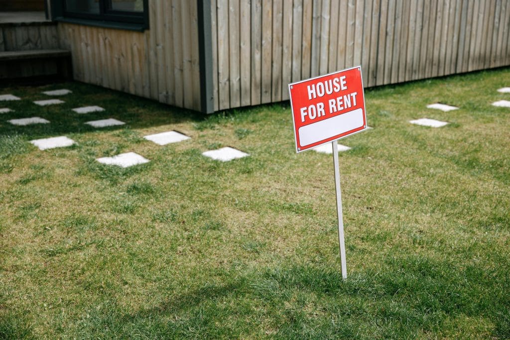 An image of a red and white house for rent sign on a lawn