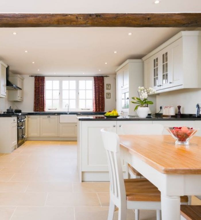 Bright and spacious kitchen with cream cabinets, a wooden dining table, a window with red curtains, and a potted plant on the counter.